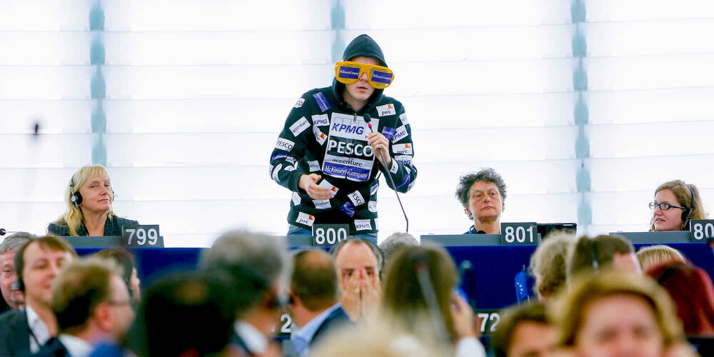 Nico speaks in the European Parliament plenary hall in Strasbourg. He’s wearing a black hoodie covered with logos of different consultancy companies.